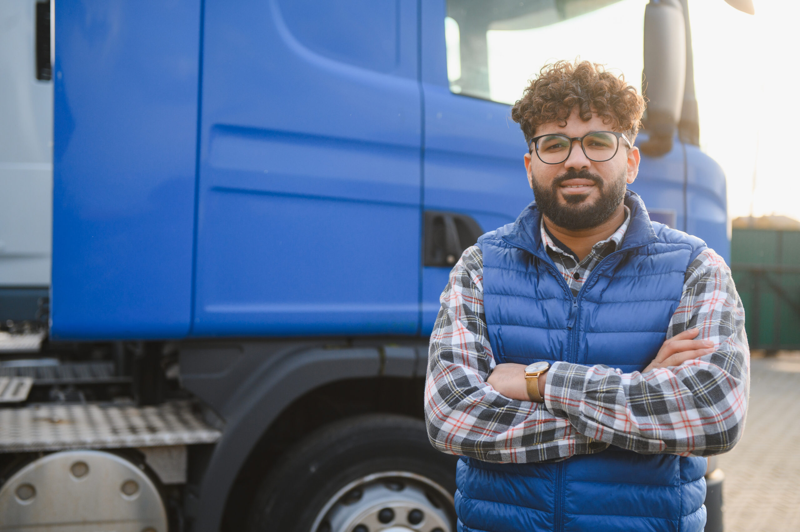 Professional truck driver standing proudly with crossed arms next to a modern blue semi truck, representing transportation and delivery